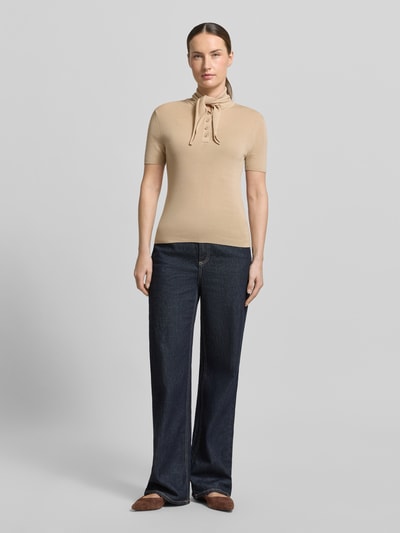 Frauenmodel trägt Modern Fit Poloshirt mit Seiden-Anteil und Schluppe von Stefanel in Beige, Glattstrick, kombiniert mit dunkler Jeans, Ganzkörperansicht von vorne. Lyocell-Mix, kurze Knopfleiste, elegante Schlichtheit.