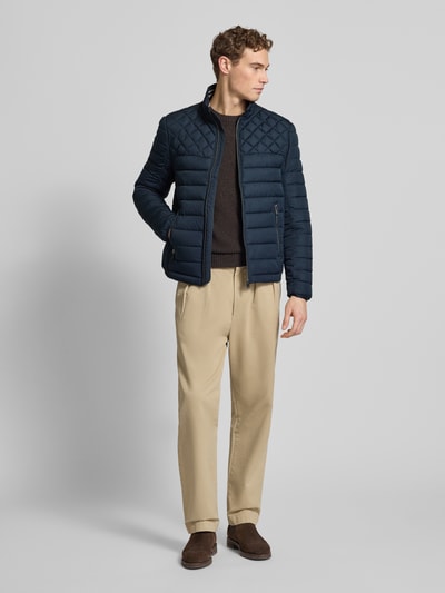 Männermodel trägt Slim Fit Steppjacke mit gefüttertem Kragen von Christian Berg Men w granatowym kolorze, krój slim fit, kieszenie zapinane na zamek błyskawiczny, podszewka na kołnierzu, elastyczne zakończenia rękawów, długość tyłu w rozmiarze M: 68 cm, szerokość ramion w rozmiarze M: 47 cm, szerokość w rozmiarze M: 52 cm, długość rękawów w rozmiarze M: 68 cm, całkowity widok z przodu