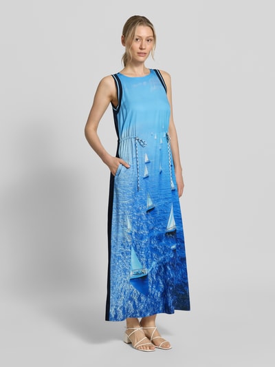 Frauenmodel trägt Maxikleid aus reinem Lyocell mit Allover-Foto-Print von Marc Cain in Blau mit taillierter Passform, Rundhalsausschnitt, Ärmelloses-Design, sichtbare Textur und Kontrastdetails, Ganzkörperansicht von vorne. Rückenlänge: 134 cm, Brustweite: 47 cm.