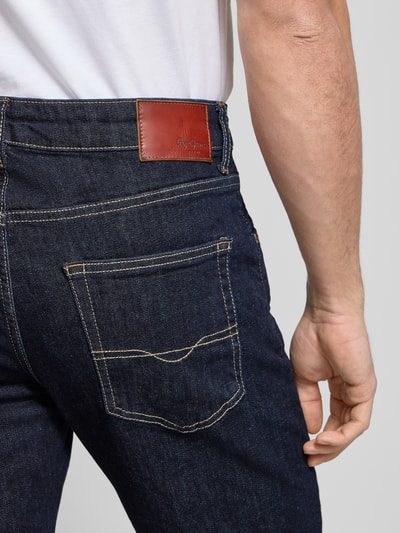 Männermodel draagt Straight Leg Jeans aus Baumwoll-Mix Modell 'CASH' van Pepe Jeans in effen donkerblauw denim met label patch, detailopname rug.