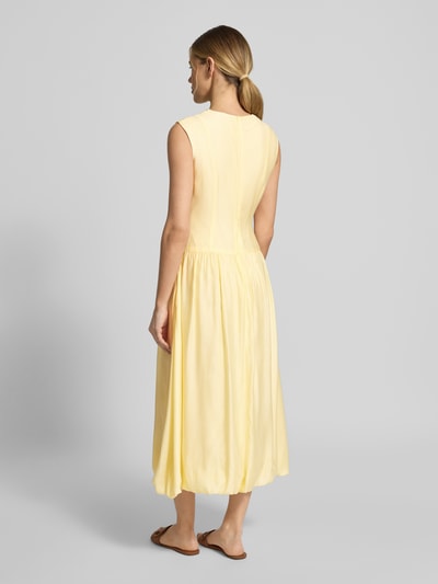 Modelka nosi Bubble Kleid mit Rundhalsausschnitt Modell 'KRISSI' od YAS, jasny żółty, długość midi, lekka tkanina z lyocellem, taliowany krój, suwak z tyłu, Szerokość w rozmiarze 36: 43 cm, długość pleców: 45 cm, widok całej sylwetki od tyłu.