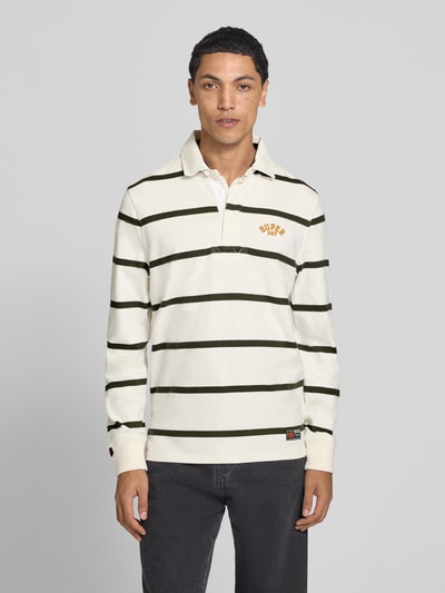 Männermodel trägt Poloshirt aus reiner Baumwolle von Superdry mit grünen Streifen, geradem Schnitt und Label-Stitching, Ganzkörperansicht von vorne.