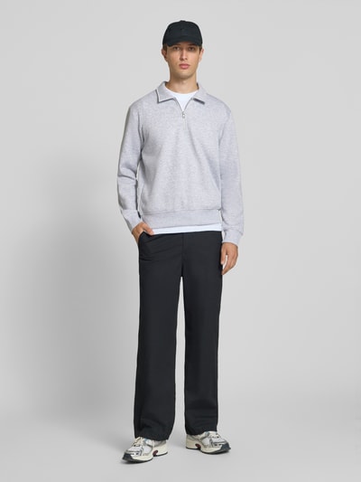 Männermodel trägt Regular Fit Sweatshirt mit Baumwoll-Anteil Modell 'Bradley' von JACK & JONES, hellgrau, glatte Textur, Troyer-Kragen, Ganzkörperansicht von vorne, Herren Sweatshirt Material-Mix, Reißverschluss, Rückenlänge 69 cm bei Größe M.