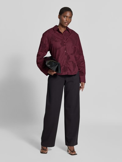 Frauenmodel trägt Oversized Hemdbluse aus reiner Baumwolle von ROTATE in Dunkelrot mit floralen Stickereien, locker geschnitten, Ganzkörperansicht von vorne.