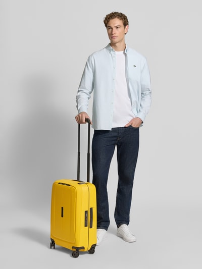 Männermodel trägt Koffer mit Strukturmuster Modell 'Spinner' von Samsonite in Gelb, Hardshell, Hauptfach mit Reißverschluss, Ganzkörperansicht von vorne.