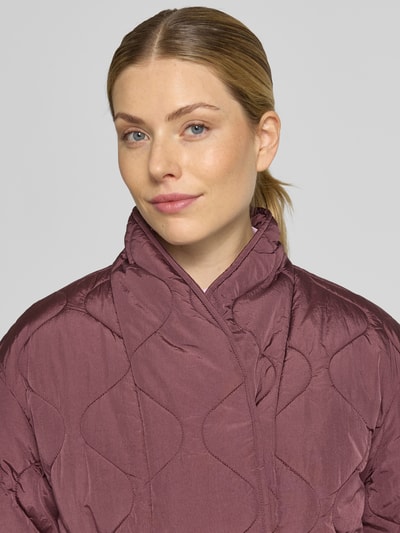 Kobieta nosi pikowaną kurtkę z wysokim kołnierzem od YAS, Steppjacke mit Bindegürtel Modell 'Himiria', kolor śliwkowy, krój regular fit, z paskiem, zbliżenie górnej części ciała.