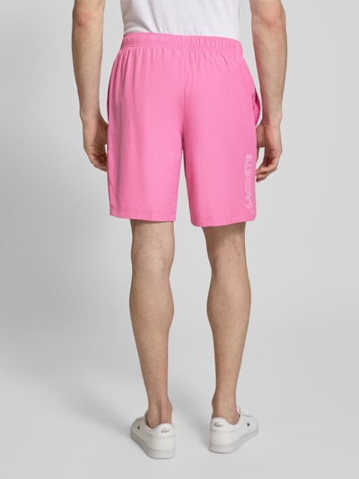 Männermodel trägt Regular Fit Sport-Shorts mit weichem Innenstoff von Lacoste Sport in Rosa mit Strukturmuster und Label Patch, Ganzkörperansicht Rückansicht.