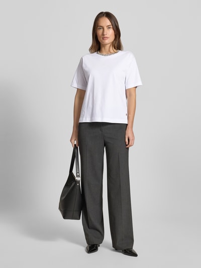 Modelka kobieca nosi białe T-shirt z detalem label JOOP! Thei, luźny krój z bawełny, okrągły ściągacz, przód całej sylwetki.