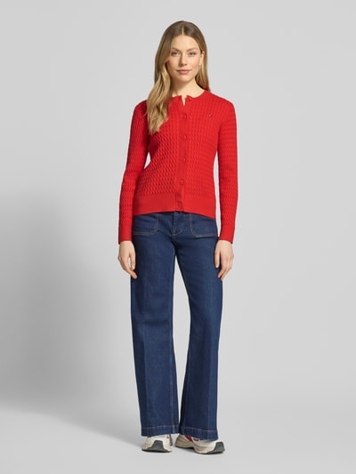 Frauenmodel trägt Slim Fit Strickjacke aus reiner Baumwolle von Tommy Hilfiger, Optik: Unifarben, Zopfmuster, Logo-Stitching, Rundhals, Langarm, gerippter Ärmel- und Rumpfabschluss, Materialverarbeitung: Strick, Ganzkörperansicht von vorne.