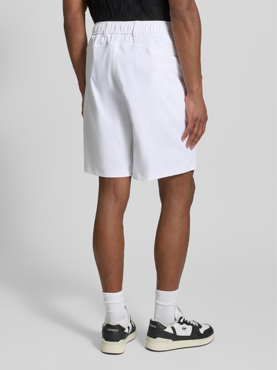 Männermodel trägt Relaxed Fit Bermudas mit Label-Schriftzug Modell 'SPIRIT70' von BOSS Green X PORSCHE, weiß, Ganzkörperansicht Rückansicht.