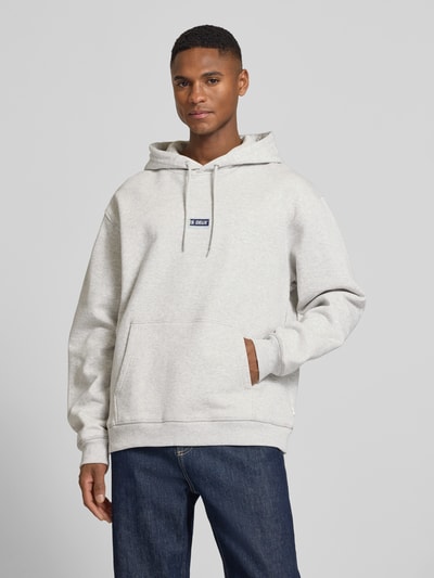 Männermodel trägt Hoodie mit Logo-Print Modell 'Chase' von Les Deux, Reine Baumwolle, Loose-Fit, Känguru-Tasche, Elastische Abschlüsse, Ganzkörperansicht von vorne.