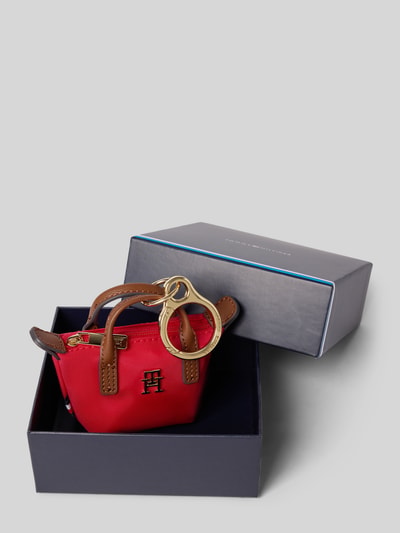 Produktfoto, Schlüsselanhänger im Henkeltaschen-Design von Tommy Hilfiger in Rot mit braunen Henkeln, Logo-Applikation aus Metall, Reißverschluss, unifarbene Optik, strukturierte Oberfläche, liegt in geöffneter Geschenkbox.