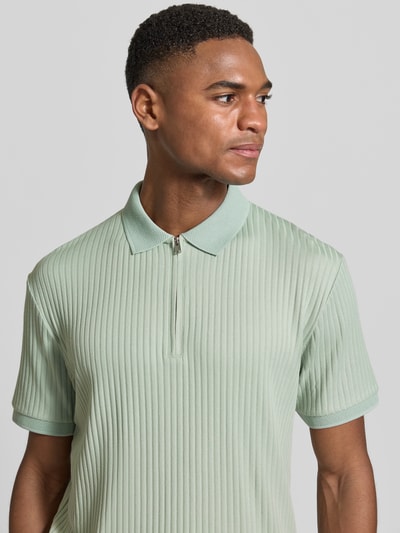 Męski model nosi Regular Fit Poloshirt mit Baumwoll-Anteil Modell 'FAVE' od SELECTED HOMME, efekt: jednolity kolor, krój regular fit, kołnierzyk polo, zapięcie: krótki zamek błyskawiczny, rękaw: krótki rękaw, zakończenie rękawów: dzianina, wykończenie materiału: prążkowana faktura, jasna zieleń, prążkowana powierzchnia, półmat, tekstura miękka, góra: przód, detal: prążki, perspektywa: zbliżenie na górną część ciała, ujęcie z przodu.