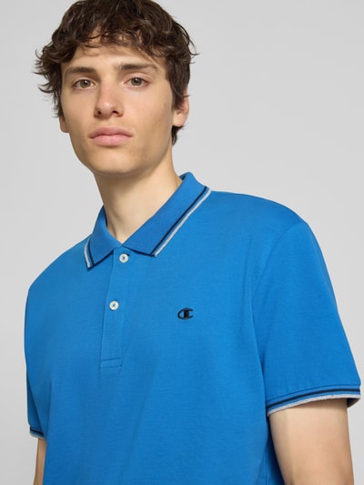 Männermodel trägt Slim Fit Poloshirt mit Label-Stitching von CHAMPION in Blau, Reine Baumwolle, Knopfleiste, Nahaufnahme Oberkörper. Rückenlänge bei Größe M: 73 cm.