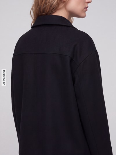 Frauenmodel trägt Loose Fit Kurzmantel aus Wolle Modell 'MAJELAA WOOL' von ARMEDANGELS in Schwarz, Filzstruktur, Ganzkörperansicht Rückansicht, KI-modifiziertes Bild