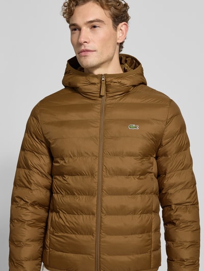 Männermodel trägt Regular Fit Bomberjacke mit Ecodown-Füllung von Lacoste in Braun, glatte Struktur, Herren Bomberjacke, Nahaufnahme Oberkörper.