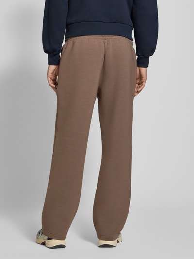 Männermodel trägt Regular Fit Sweatpants aus Material-Mix Modell 'BILL LEGACY' von JACK & JONES, braun, Elastikbund, Ganzkörperansicht Rückansicht, Herren Sweatpants, Eingrifftaschen, Innenbeinlänge 77 cm, KI-modifiziertes Bild.