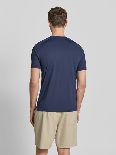 Männermodel trägt T-Shirt mit Label-Print von EA7 Emporio Armani in Dunkelblau, Slim-Fit, Material-Mix mit Stretch-Anteil, Ganzkörperansicht Rückansicht.
