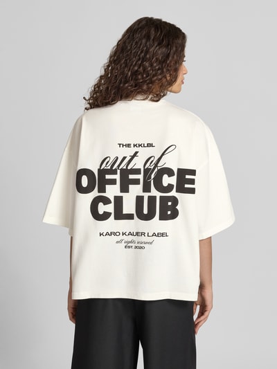 Kobieta nosi Cropped Oversized T-Shirt mit Label-Print od Karo Kauer, damski t-shirt z bawełny, oversize, krój krótki, nadruk z logo z przodu i z tyłu, okrągły dekolt, długość tyłu w rozmiarze S: 60 cm, tył, całkowity widok sylwetki od tyłu