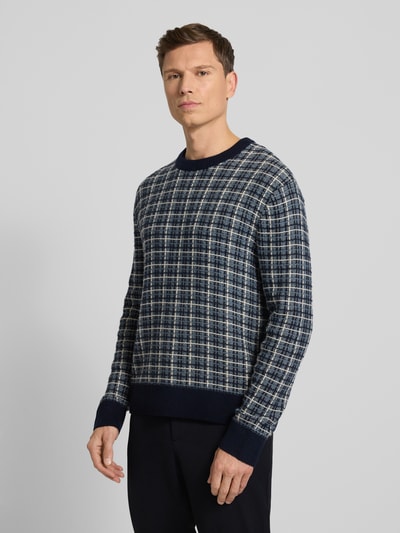 Männermodel draagt Regular Fit Strickpullover aus Woll-Mix Modell 'MIKOLAS' van SELECTED HOMME met all-over ruitpatroon in blauw en grijs, geribde boorden, lange mouwen, gebreide textuur. Ganzkörperansicht von vorne.