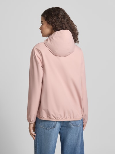 Modelka nosi Regular Fit Windbreaker mit Logo-Applikation od Superdry, jasnoróżowy, kaptur z troczkiem, widok całej sylwetki z tyłu. Długość pleców w rozmiarze S: 25 cm, szerokość ramion w rozmiarze S: 44 cm, szerokość w rozmiarze S: 49 cm, długość rękawa w rozmiarze S: 65 cm.