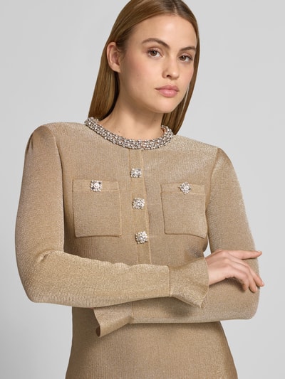Frauenmodel trägt Minikleid mit Viskose-Anteil von Self-Portrait in Goldton mit Ziersteinbesatz und aufgesetzten Taschen, Nahaufnahme Oberkörper. Taillierte Passform, Baumwoll-Mix, langärmelig, feine Textur.