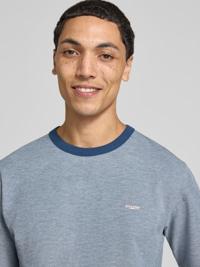 Männermodel trägt Regular Fit T-Shirt aus Baumwoll-Mix Modell 'Alves' von JACK & JONES, meliertes Blau, Logo-Detail, Nahaufnahme Oberkörper.
