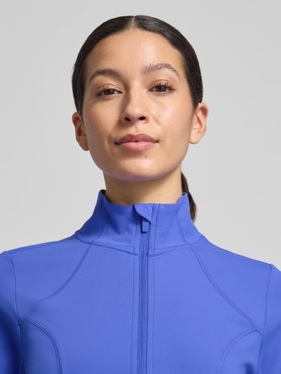 Kobiece model prezentuje Slim Fit Jacke mit Stehkragen Modell 'Storm' od Fabletics, niebieski kolor, krój slim fit, krótki fason, długi rękaw z otworem na kciuk, Szerokość w rozmiarze S: 42 cm, Szerokość ramion w rozmiarze S: 36 cm, Długość tyłu w rozmiarze S: 44 cm, Długość rękawa w rozmiarze S: 74 cm, zbliżenie na górną część ciała