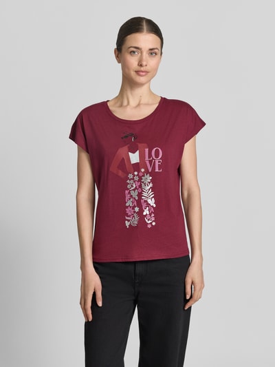Kobiece modelka nosi T-Shirt mit Motiv-Print und Rundhalsausschnitt von Christian Berg Woman, bawełna-wiskoza, krój regular fit, nadruk z motywem, kolor bordowy, długość tyłu w rozmiarze S: 55 cm, pełny przód, gładka tekstura, całkowite ujęcie sylwetki z przodu.