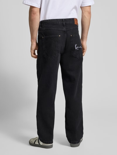 Männermodel trägt Baggy Jeans im 5-Pocket-Design mit Logo-Stitching von KARL KANI, reine Baumwolle, schwarze Farbe, Ganzkörperansicht Rückansicht.