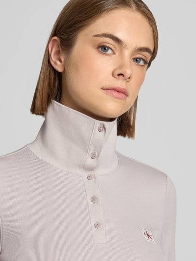 Frauenmodel trägt Slim Fit Langarmshirt aus Baumwoll-Mix von Calvin Klein Jeans in hellem Beige mit Struktur und Logo, Nahaufnahme Oberkörper.