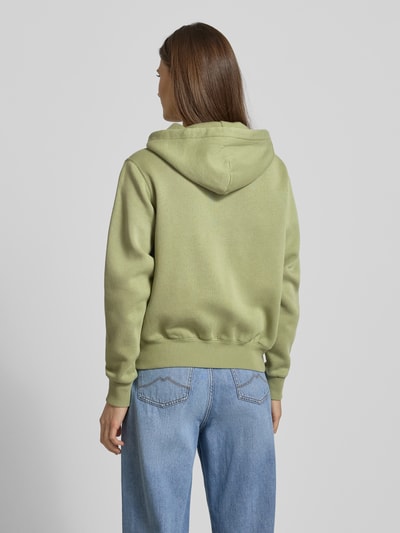 Kobiece modelka nosi bluzę rozpinaną z kapturem od Polo Ralph Lauren z mieszanki bawełny, luźny krój, wpuszczane kieszenie, wyhaftowane logo, tunel, zamek błyskawiczny, prążkowane wykończenia w kolorze oliwkowym, widok całej sylwetki od tyłu.
