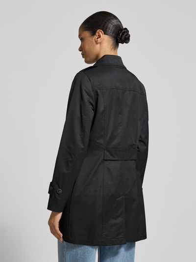Frauenmodel trägt schwarzen Trenchcoat mit Ärmelriegeln von Fuchs Schmitt, glatte Textur, Eingrifftaschen, Ganzkörperansicht Rückansicht.