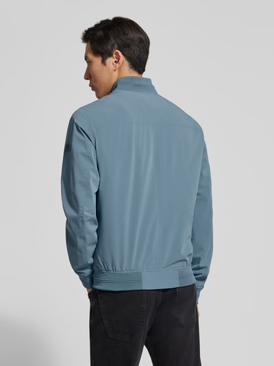 Männermodel trägt Regular Fit Bomberjacke mit Stehkragen van Guess in blauw met elastische boorden, steekzakken, rits, rugaanzicht, context: heren bomberjack van Guess met regular fit, steekzakken, ritssluiting, elastische boorden, ruglengte maat M 67 cm, schouderbreedte 46 cm, borstbreedte 55 cm, mouwlengte 67 cm. Ganzkörperansicht Rückansicht.
