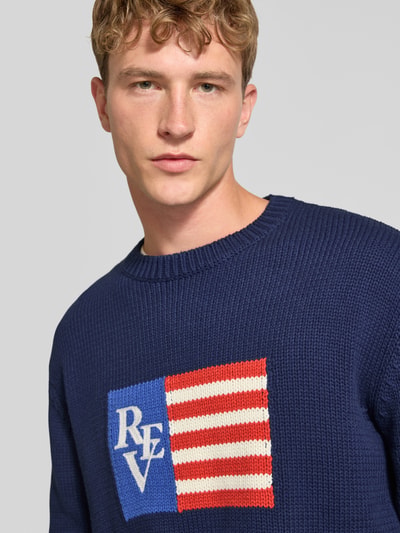 Männermodel trägt Regular Fit Strickpullover aus Baumwoll-Mix von REVIEW, dunkelblau mit Motiv-Stitching und Rundhalsausschnitt, Nahaufnahme Oberkörper.