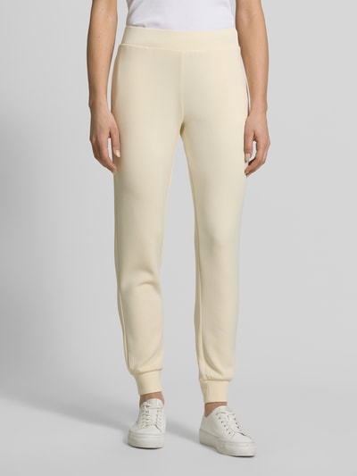 Frauenmodel trägt Sweatpants mit Label-Detail Modell 'OLYMPE' von Guess Activewear in Beige, körpernaher Schnitt, seitliche Eingrifftaschen, elastischer Bund, Material-Mix mit Stretch, Ganzkörperansicht von vorne.