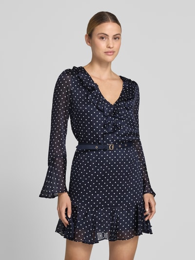 Vrouwenmodel draagt Minikleid met Rüschenbesatz van GUESS in donkerblauw met witte stippen, getailleerd, V-hals, met lange mouwen, afneembare tailleriem, ruglengte maat S 83 cm, borstwijdte 42 cm, mouwlengte 62 cm, textuur licht en transparant. Nahaufnahme oberkörper.