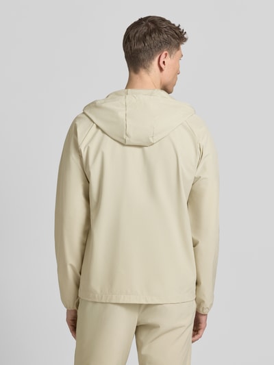 Męski model nosi Regular Fit Jacke mit Logo-Print Modell 'Vibe' von Under Armour, beżowy kolor, elastyczny materiał, kaptur ze sznurkiem, kieszenie, długość tyłu w rozmiarze M: 70 cm, długość rękawa w rozmiarze M: 72 cm, widok całej sylwetki z tyłu.