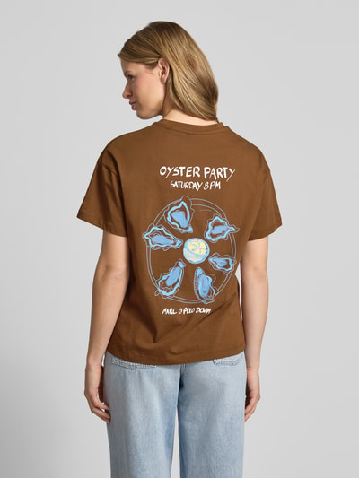 Frauenmodel trägt Relaxed Fit T-Shirt aus reiner Baumwolle - Special Drop von Marc O'Polo Denim, Optik: Unifarben, Rückenprint, Label-Print, Rundhals, Kurzarm, reine Baumwolle, braun mit hellem Print, Ganzkörperansicht Rückansicht.