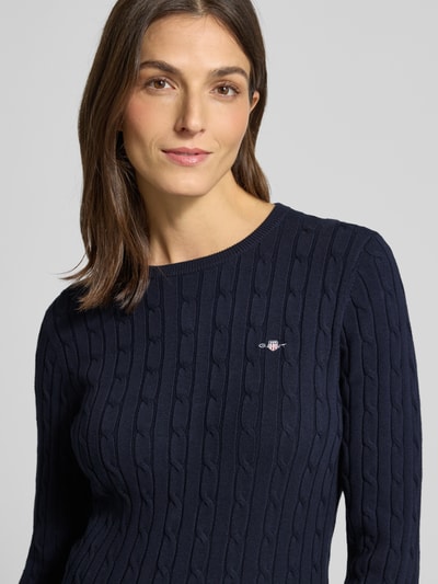 Frauenmodel trägt Strickpullover mit Label-Detail von GANT, unifarbenes Design in Dunkelblau, Strukturmuster, Rundhalsausschnitt, Baumwoll-Mix mit Stretch-Anteil, körpernaher Schnitt, gerippte Abschlüsse, Nahaufnahme Oberkörper.