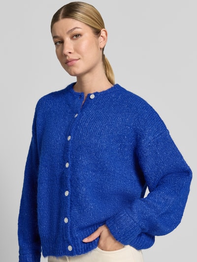 Modelka nosi kardigan rozpinany Relaxed Fit Strickjacke mit Woll-Anteil Model 'Belablue' od ICHI, elastyczna mieszanka materiałów z dodatkiem wełny, okrągły dekolt, listwa guzikowa, długi rękaw, prążkowane ściągacze, długość tyłu 57 cm, długość rękawów 71 cm, widok z przodu na górną część sylwetki.