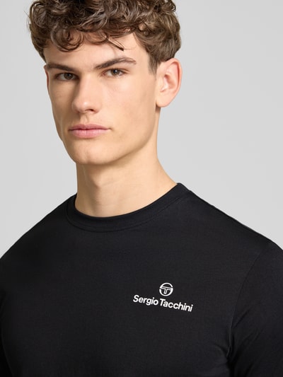 Męski model nosi Regular Fit T-Shirt mit Logo-Print von Sergio Tacchini, czarny kolor, czysta bawełna, dekolt okrągły, krój regular fit, długość pleców w rozmiarze M: 69 cm, zbliżenie na górną część ciała.