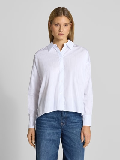 Kobiecy model nosi Relaxed Fit Bluse mit verlängertem Rückenteil Modell 'CLOELIA' von Drykorn z bawełny, kołnierzyk koszulowy, biała, prostokątne kształty, tekstura gładka, długość tyłu 66 cm, długość rękawów 52 cm, krój relaxed fit, przód krótszy, widoczne guziki, widok całej sylwetki z przodu.
