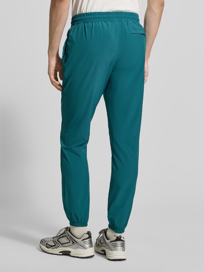 Männermodel trägt Regular Fit Jogger mit Logo-Print Modell 'Vibe' von Under Armour in Türkis, elastischer Bund, Ganzkörperansicht Rückansicht.