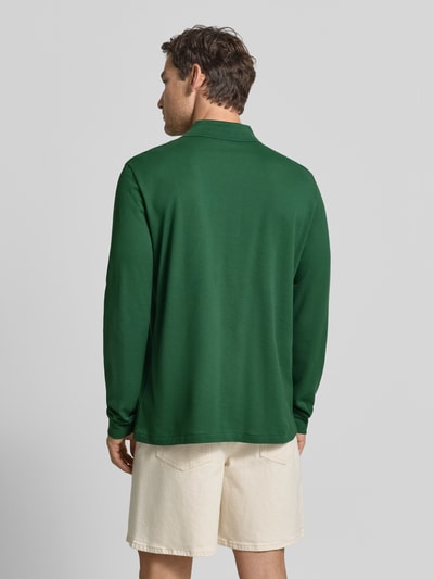 Männermodel trägt Regular Fit Poloshirt aus reiner Baumwolle von Lacoste in Dunkelgrün, helle Shorts, Ganzkörperansicht Rückansicht.