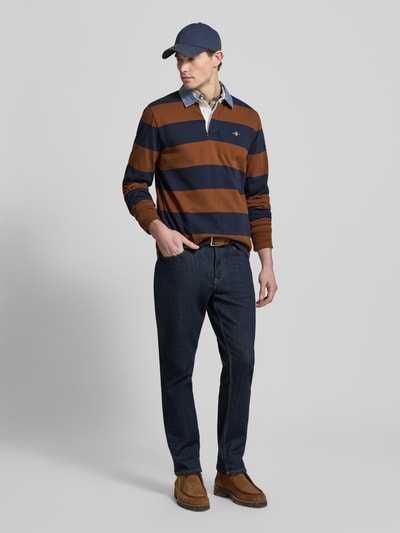 Męski model nosi Bluza Sweatshirt mit Label-Stitching od Gant w pasy, bawełna, krój regular fit, kołnierzyk polo, długie rękawy, długość tyłu 72 cm, długość rękawów 66 cm, prążkowane zakończenia rękawów, haftowane logo, widok całej sylwetki z przodu.