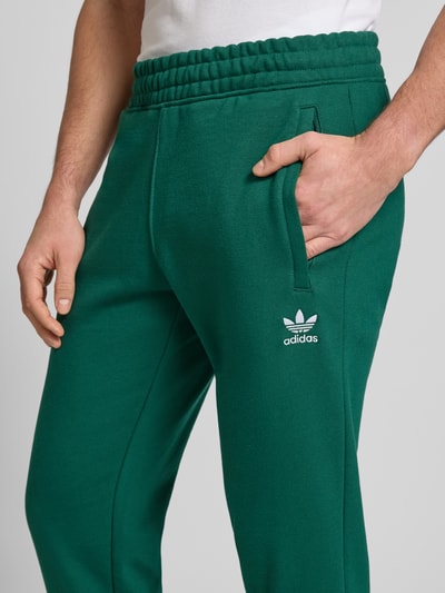 Männermodel trägt grüne Sweatpants mit elastischem Bund von adidas Originals, Baumwoll-Mix, Label-Stitching, Nahaufnahme Oberkörper.