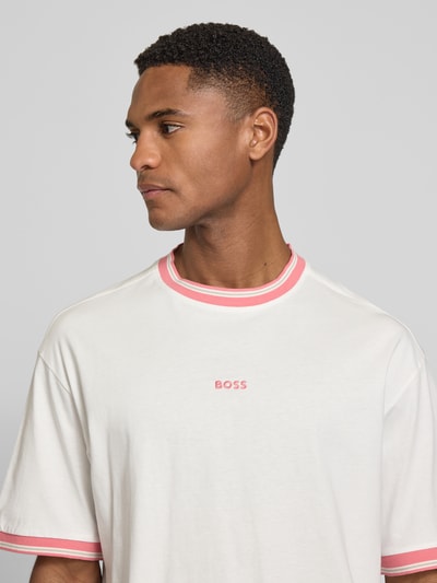 Männermodel trägt Regular Fit T-Shirt aus reiner Baumwolle Modell 'TE_BLOCKS' von BOSS Orange in Weiß mit rosa Details, Nahaufnahme Oberkörper.