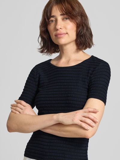 Frauenmodel trägt T-Shirt aus Viskose-Mix mit Rundhalsausschnitt von Emporio Armani, Strukturmuster in Schwarz, Nahaufnahme Oberkörper.