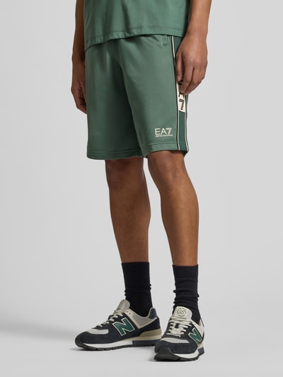 Mężczyzna nosi Szorty mit Logo und Eingrifftaschen von EA7 Emporio Armani, krój relaxed fit, elastyczny pas, wpuszczane kieszenie, logo. Ganzkörperansicht z przodu. Szerokość w rozmiarze M: 42 cm, długość wewnętrzna nogawki: 28 cm.